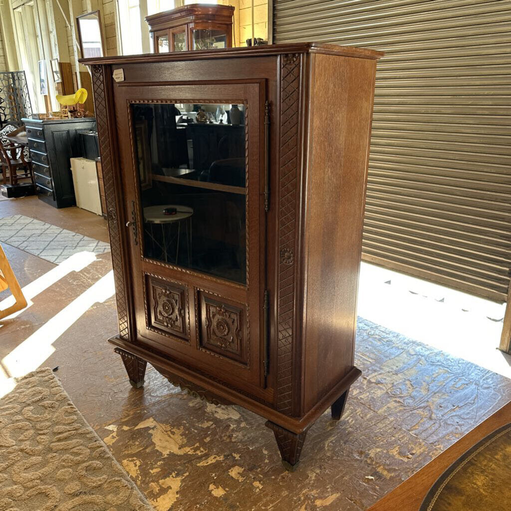 Wooden cabinet with glass doors in a room with a carpeted floor and a window.