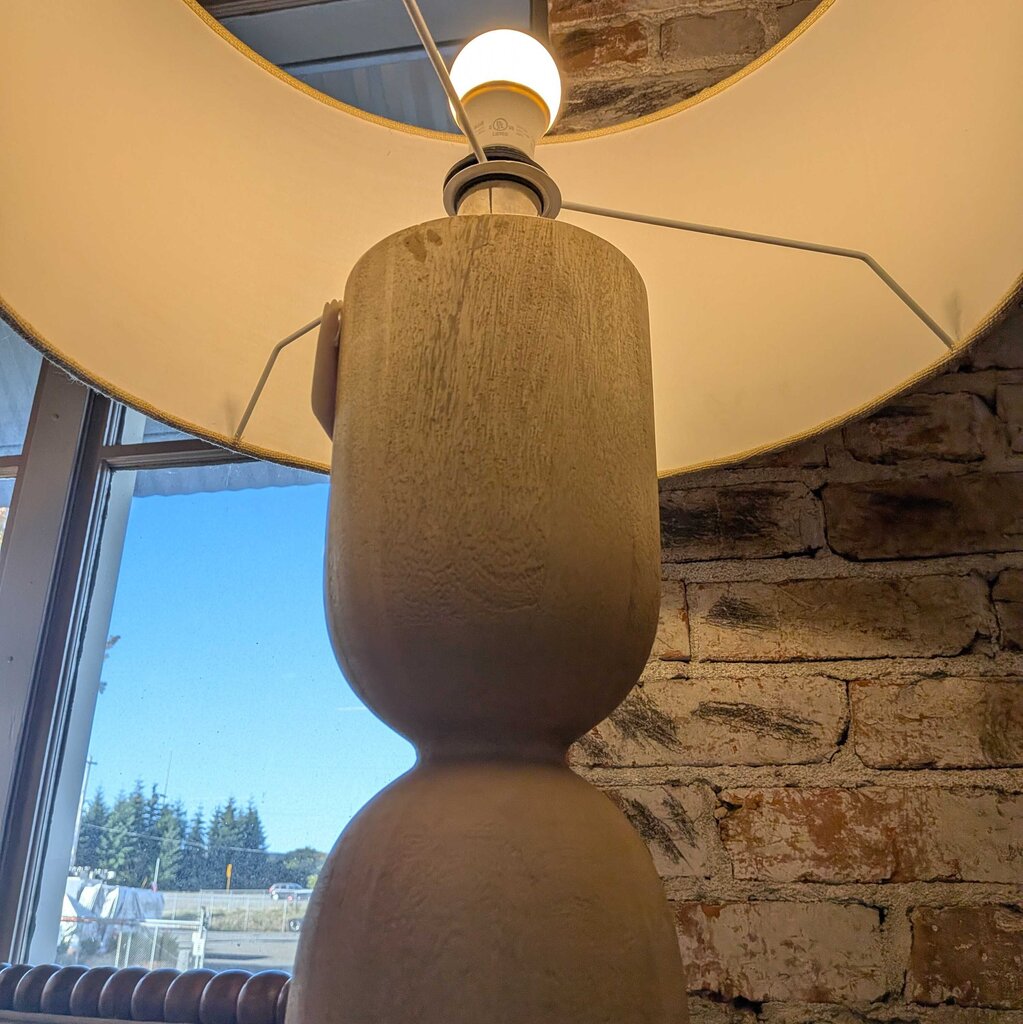Decorative lamp with textured base and white shade against a stone wall.