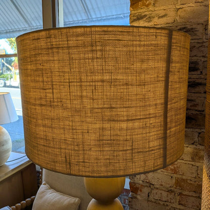 Textured brown lampshade on a yellow base against a brick wall.