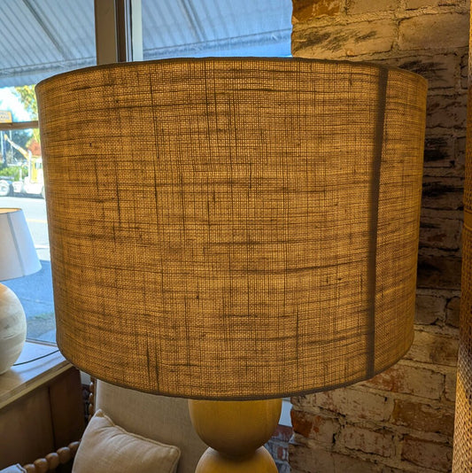 Textured brown lampshade on a yellow base against a brick wall.