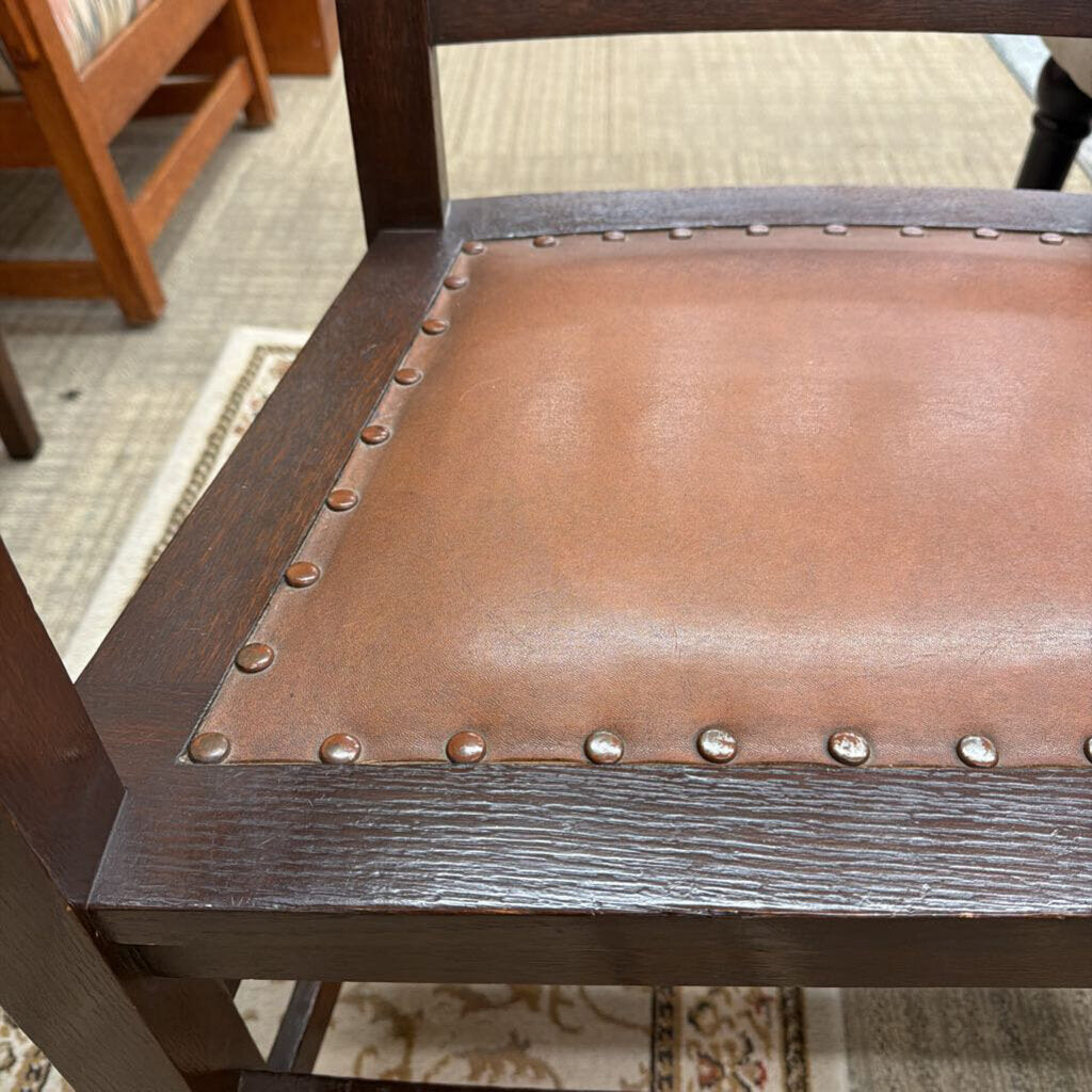 Close-up of a chair with brown leather seat and wooden frame, on a carpeted floor.