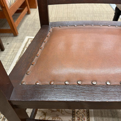 Close-up of a chair with brown leather seat and wooden frame, on a carpeted floor.
