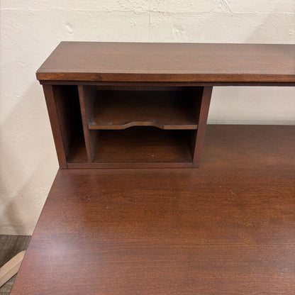 Wooden desk with a shelf against a plain wall