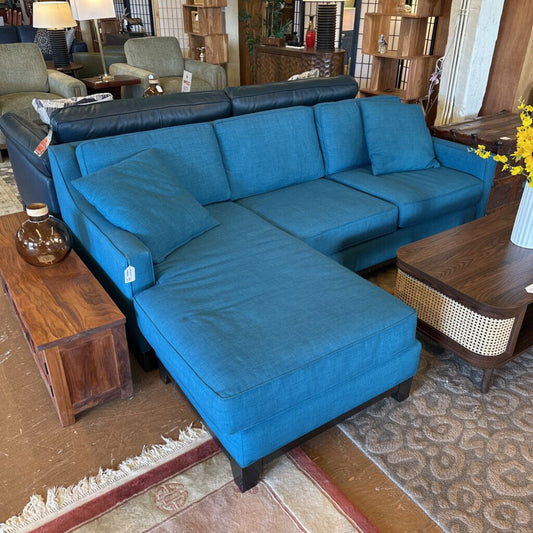 Blue sectional sofa in a furniture store with wooden tables and decor items.