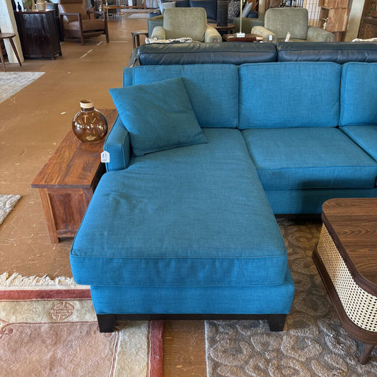 Blue sectional sofa in a room with wooden furniture and rugs.