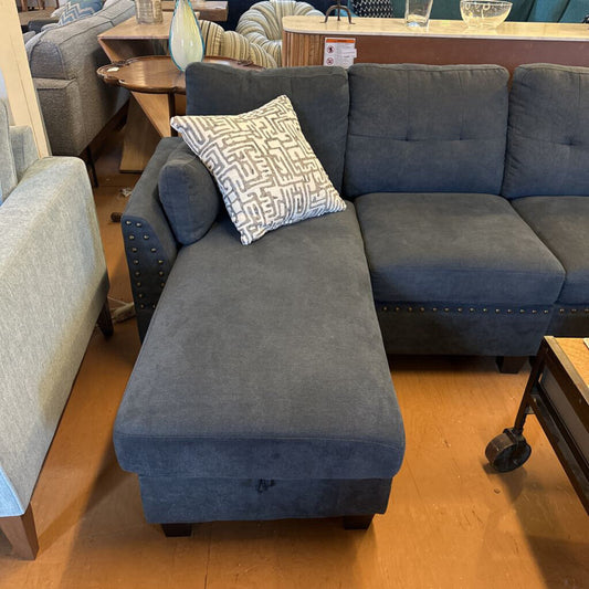Gray sectional sofa with a patterned pillow in a furniture store setting.