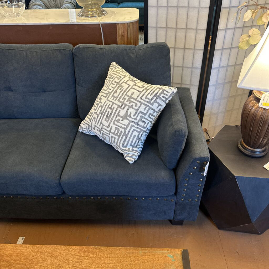 Blue sofa with a patterned pillow in a room setting with a side table and lamp.