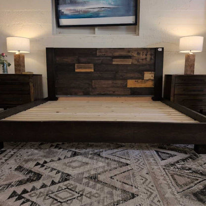 Wooden bed frame in a room with a patterned rug and wall art.