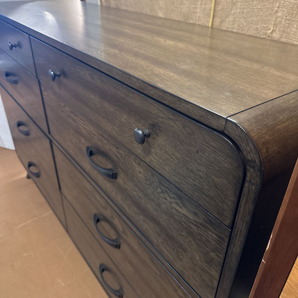 Wooden dresser with multiple drawers and metal handles on a wooden floor.