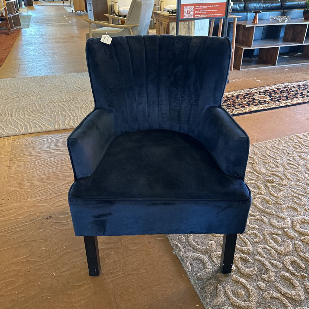 Blue velvet armchair in a showroom setting with flooring and furniture visible.