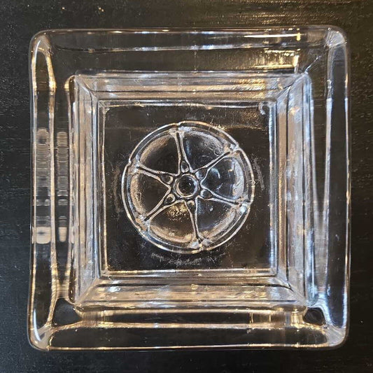 Clear glass ashtray with a wheel design on a black background