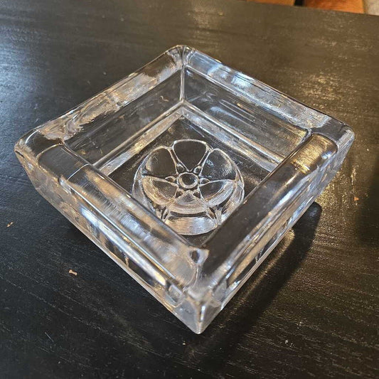 Clear glass ashtray with decorative center on a dark surface