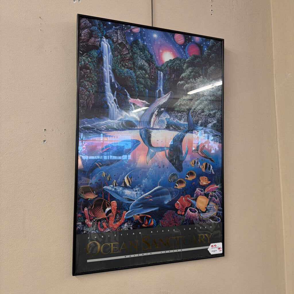 Framed artwork of an ocean scene with dolphins and marine life on a beige wall.
