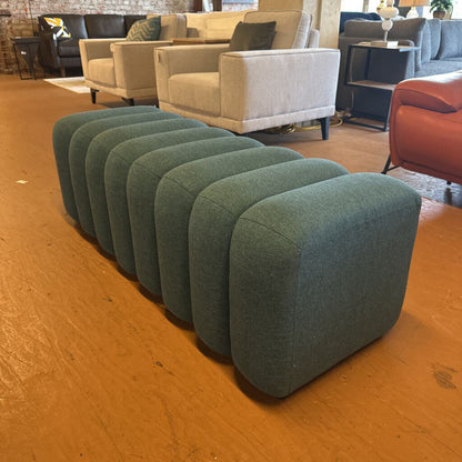 Row of green ottomans on a wooden floor with blurred furniture in the background
