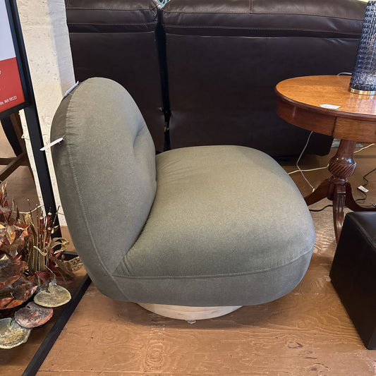 Gray chair in a room with a brown leather couch and wooden table.