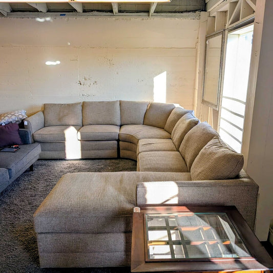 Beige sectional sofa in a living room with wooden walls and a window.