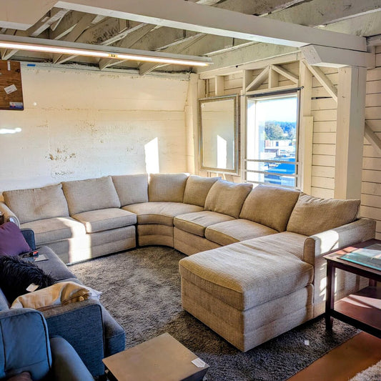 Beige sectional sofa in a room with wooden walls and a window.