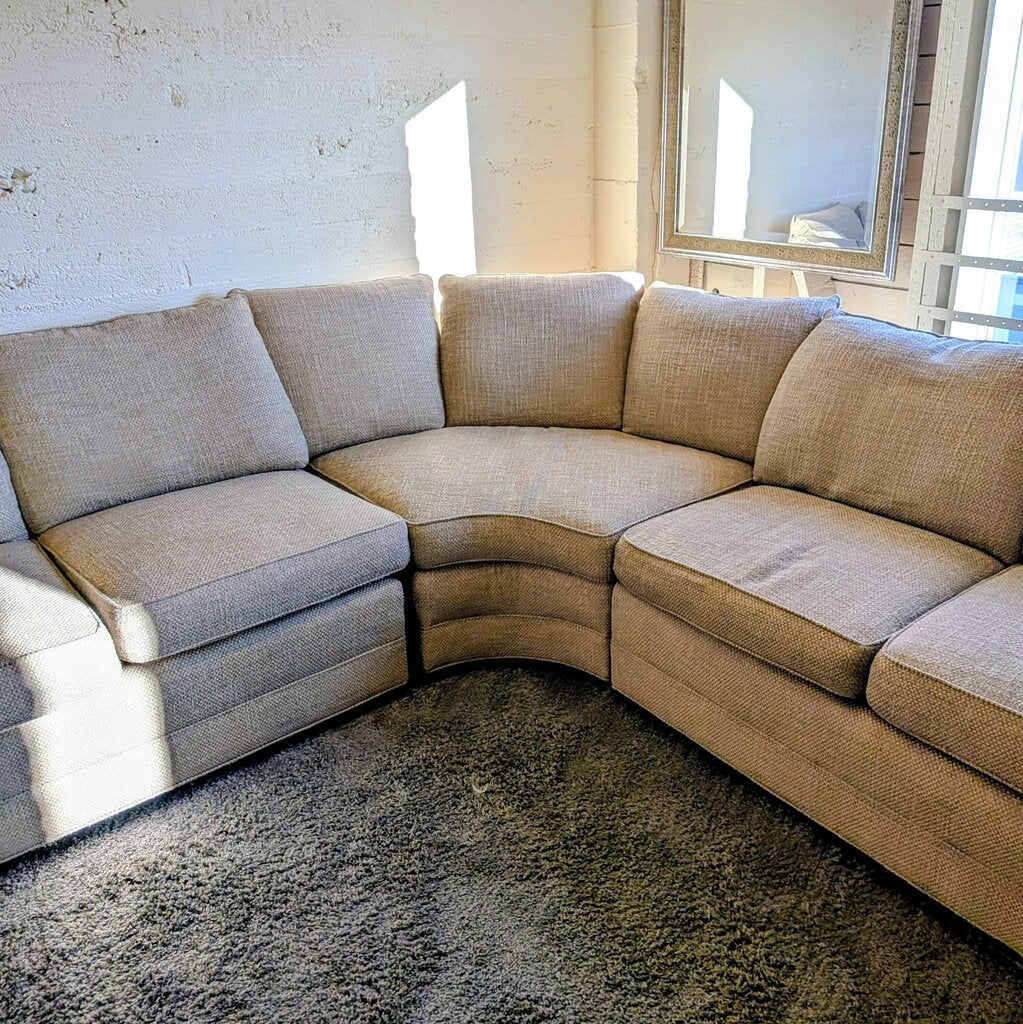 Beige sectional sofa in a room with large windows and a textured wall.