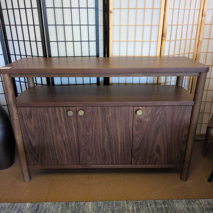 Wooden sideboard with two doors against a decorative wall.