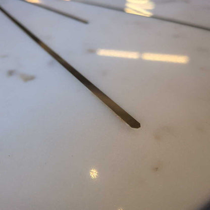 Close-up of a thin metal rod on a white surface with reflections