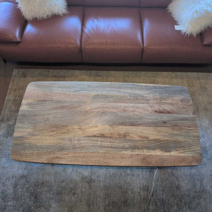 Wooden cutting board on a gray surface with a brown leather couch in the background