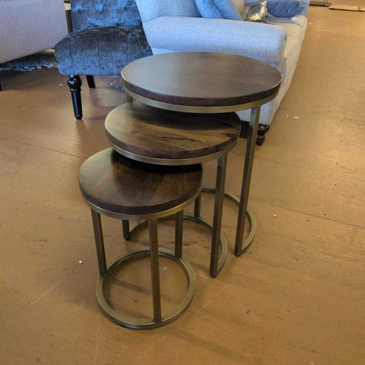Set of three wooden nesting tables on a wooden floor with furniture in the background