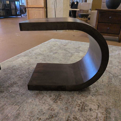 Modern dark wood coffee table with a curved design on a patterned rug.