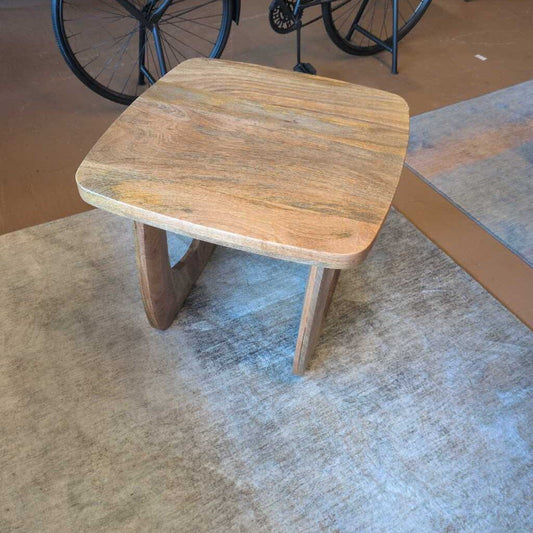 Wooden side table on a concrete floor with a bicycle in the background
