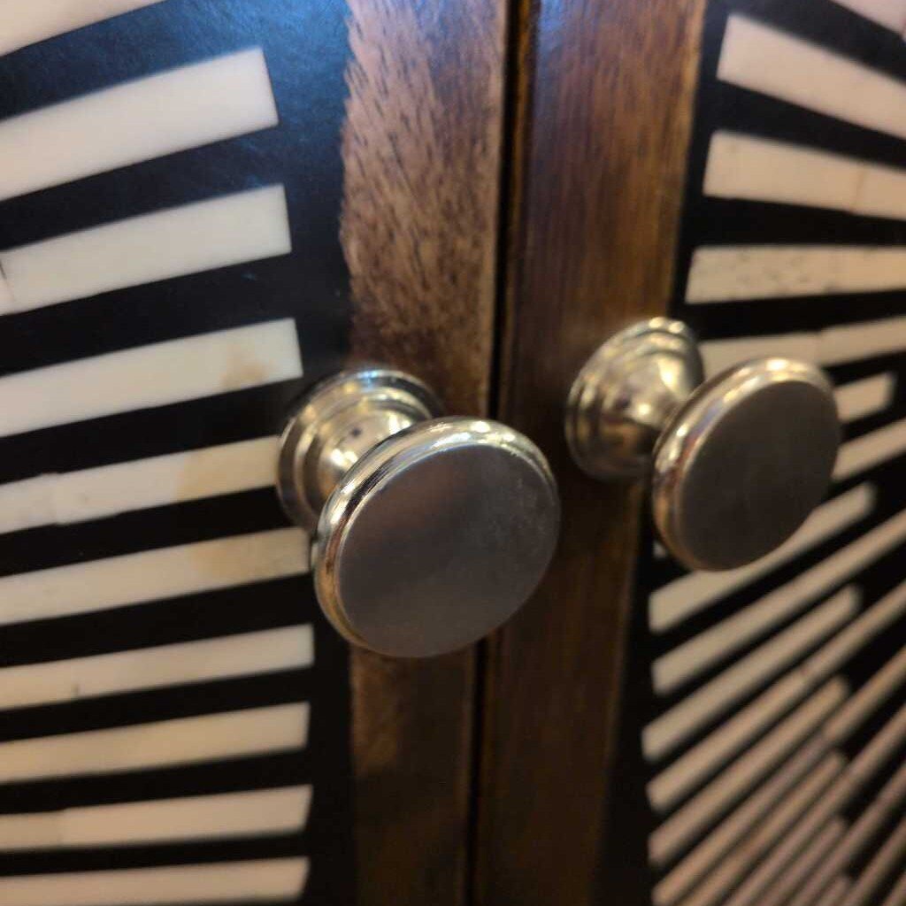 Close-up of a wooden cabinet with metal knobs on a black and white striped background