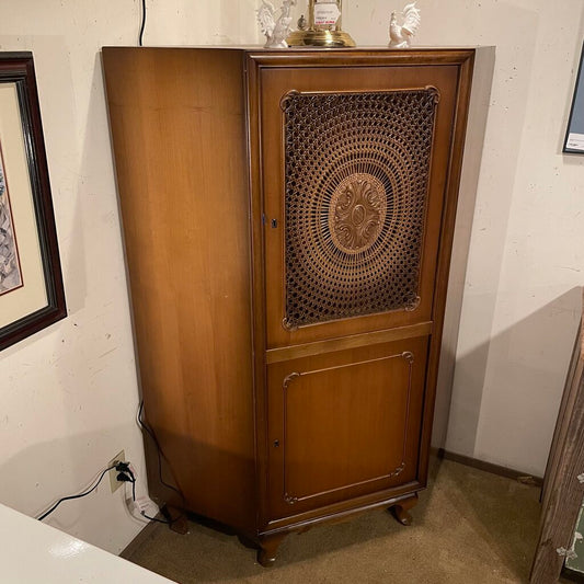 The piece features a unique pentagonal footprint that fits seamlessly into a corner, maximizing floor space while providing significant vertical storage. The upper section is defined by a single large door featuring a striking circular cane insert.