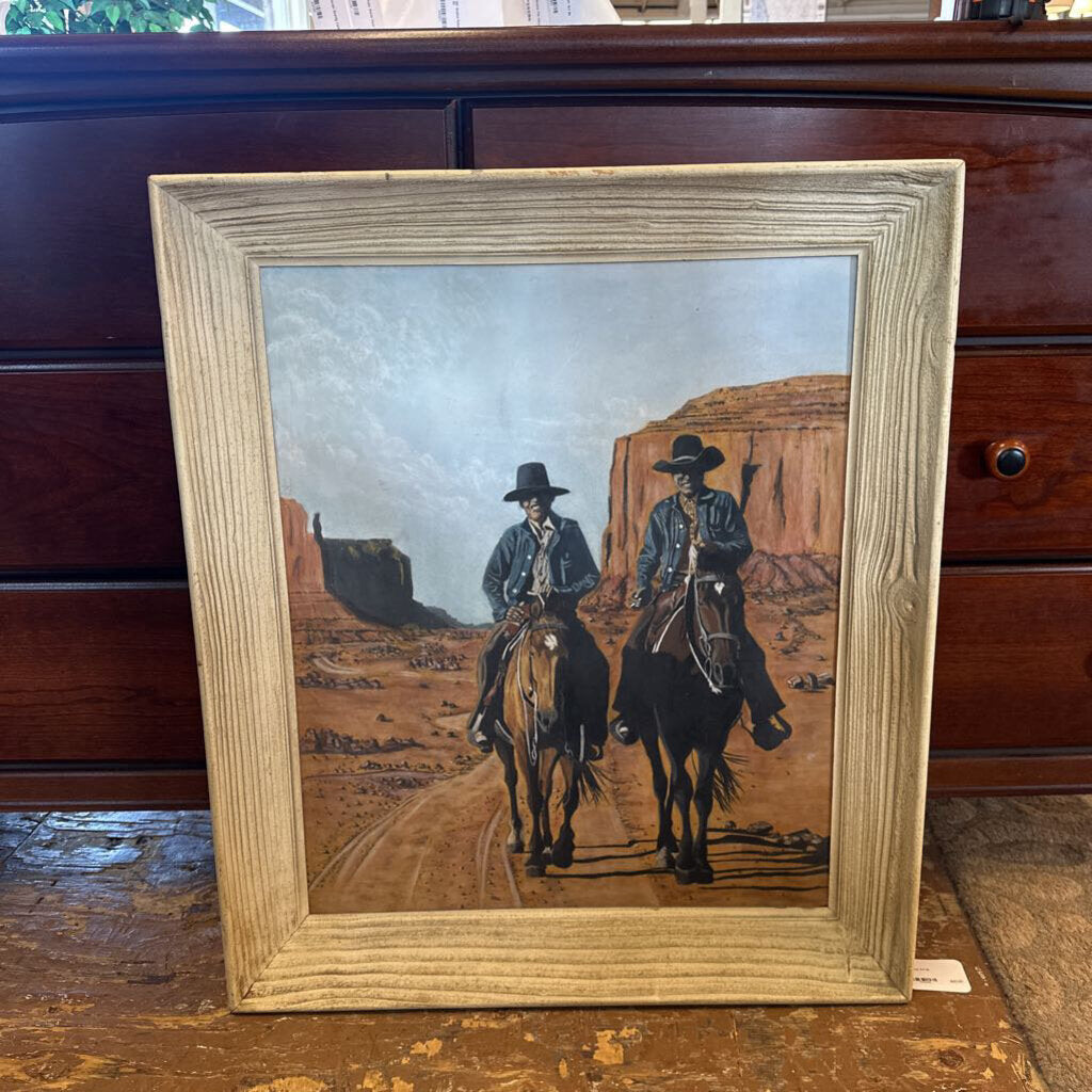 Framed painting of two cowboys on horses in a desert landscape.