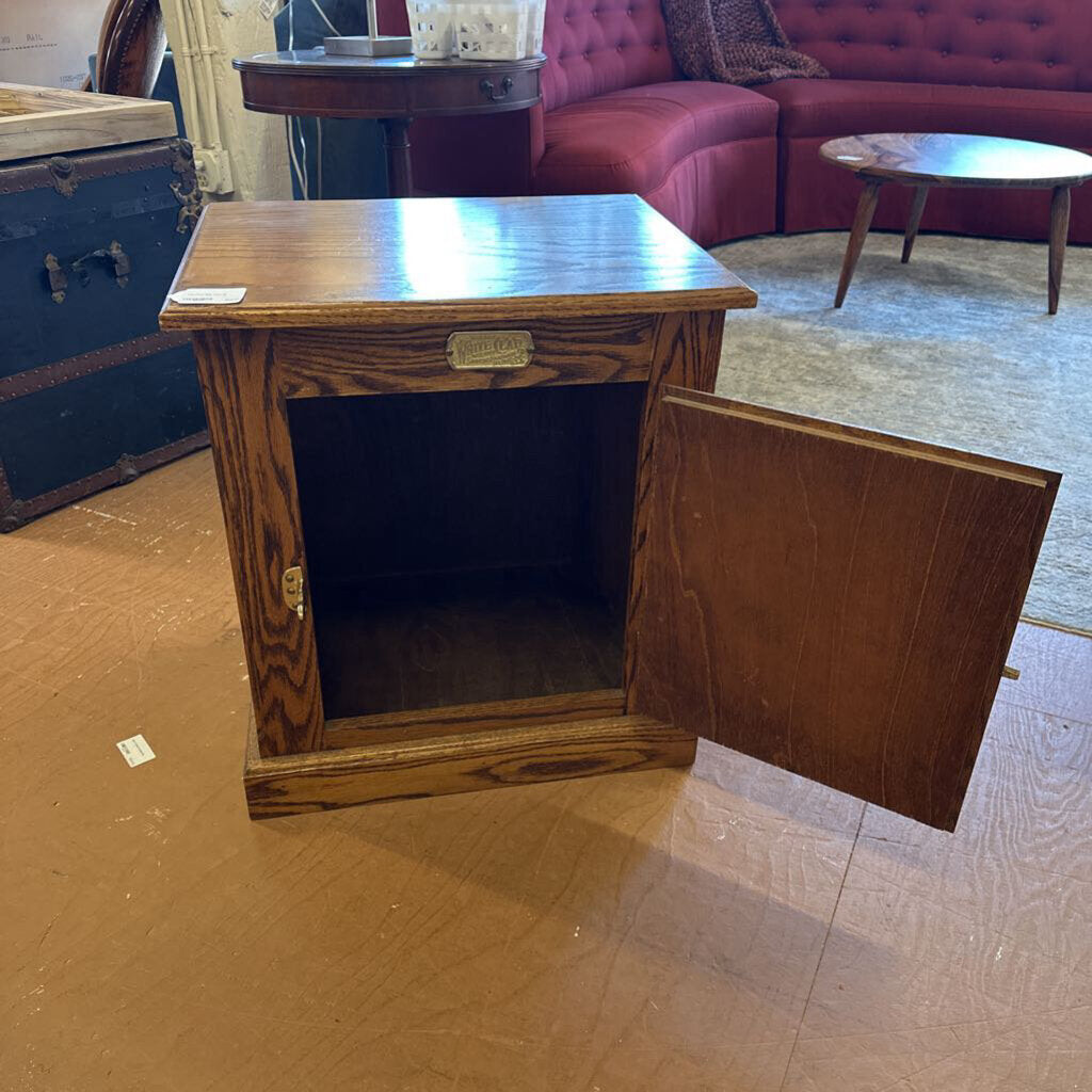 Wooden cabinet with open door on a wooden floor, with a red sofa and other furniture in the background.