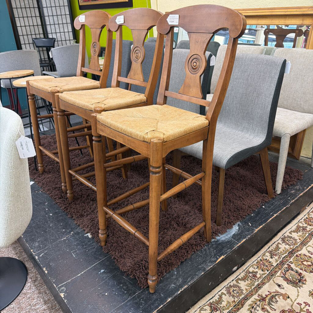 Three wooden bar stools with cushioned seats in a showroom setting.