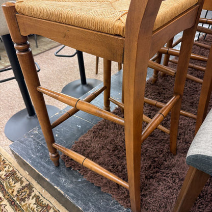 Wooden bar stool with a woven seat on a textured floor