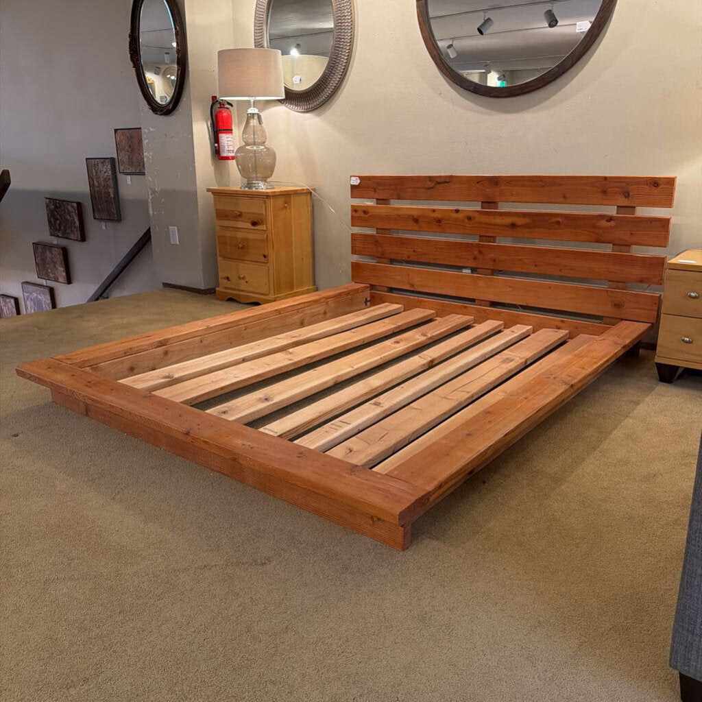 Wooden bed frame in a room with mirrors and a lamp.