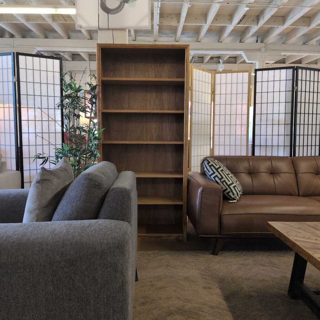 Living room with gray sofa, brown leather couch, wooden bookshelf, and decorative pillows.