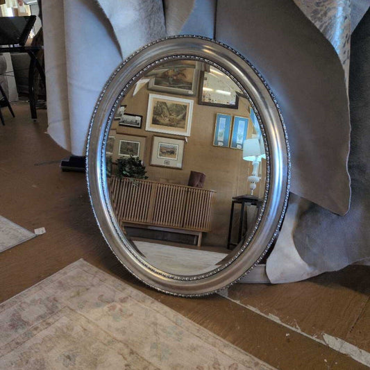 Round silver mirror reflecting a room with framed pictures on the wall.