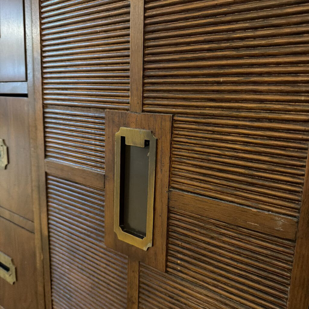 Close-up of a wooden door with a textured pattern and a rectangular gold handle.