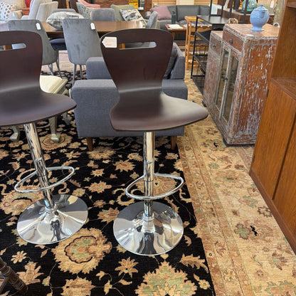 Two dark brown bar stools with chrome bases on a patterned rug in a room with furniture.