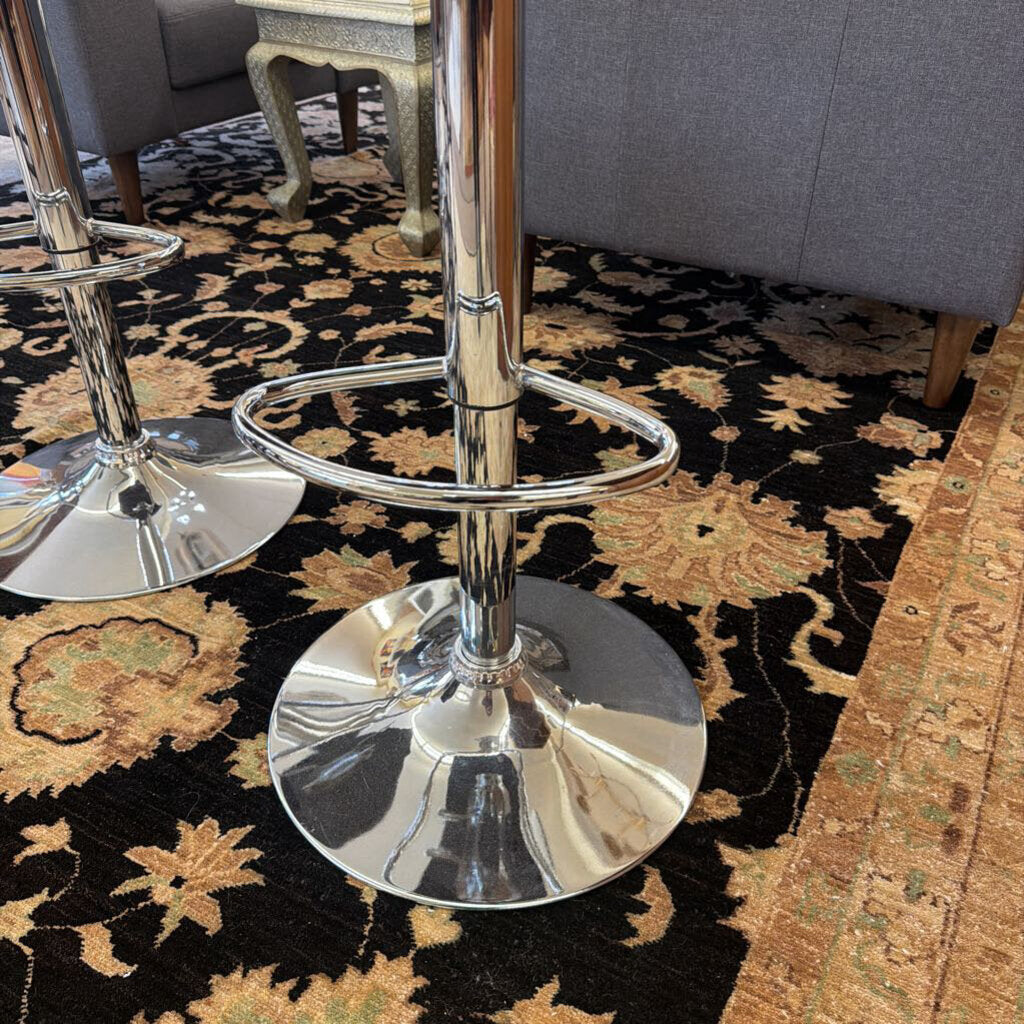 Chrome bar stools on a patterned rug with a gray sofa in the background