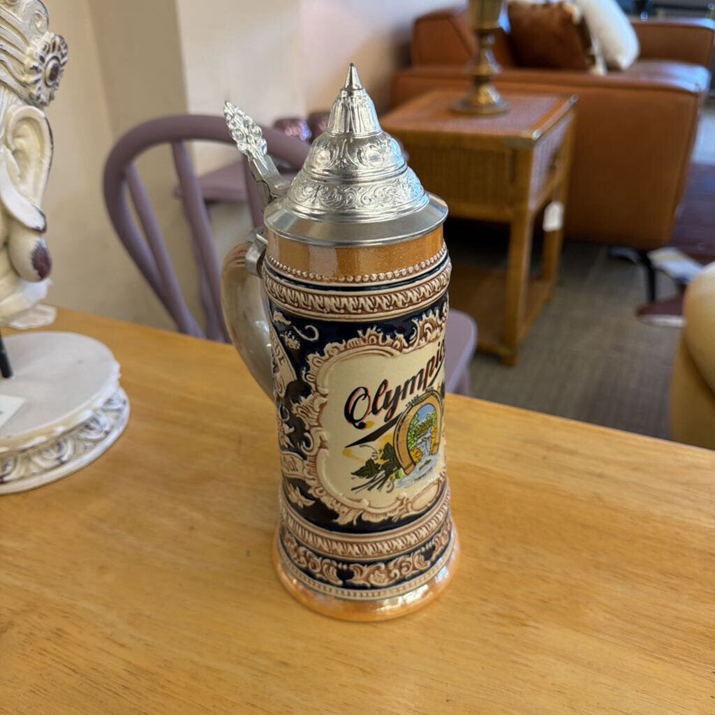 Decorative beer stein with 'Olympia' branding on a wooden table.