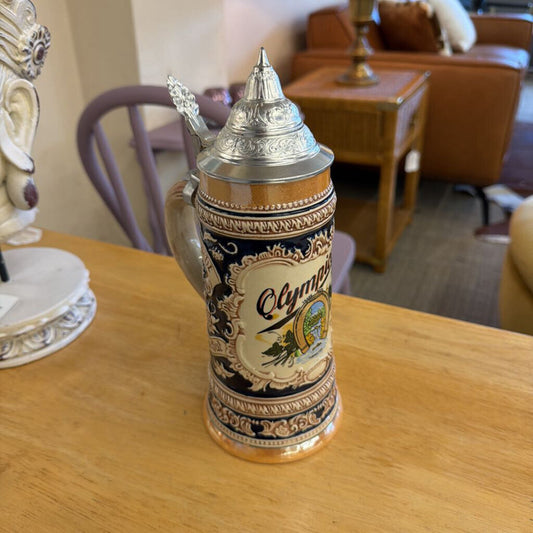 Decorative beer stein with 'Olympia' branding on a wooden table.