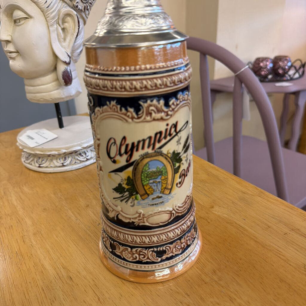 Decorative beer stein with 'Olympia' branding on a wooden table.