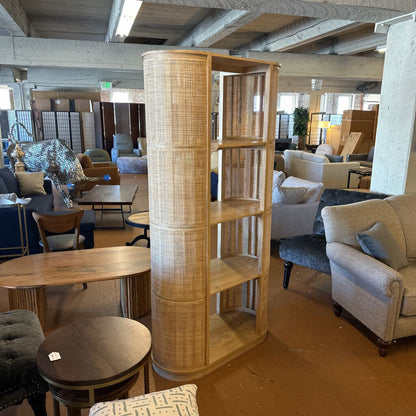 Wooden bookshelf in a furniture store with various seating and decor items.