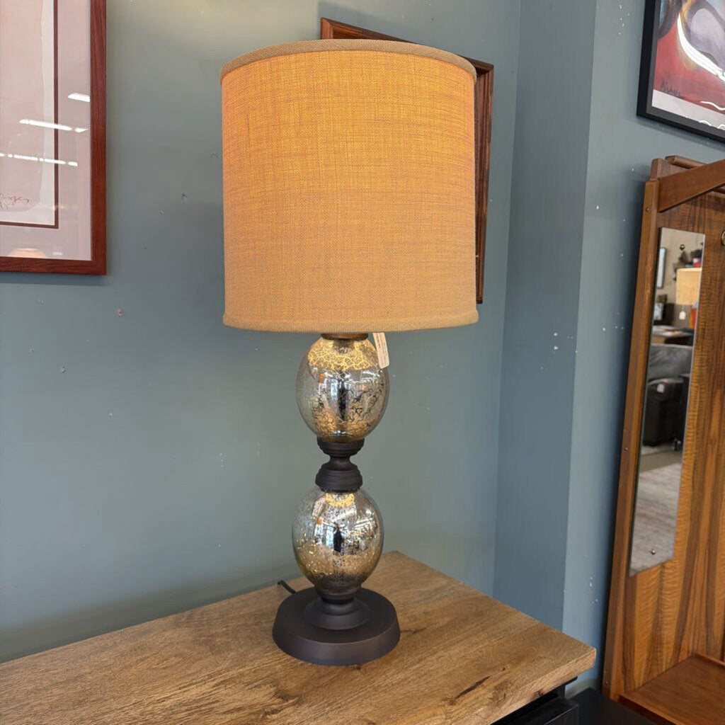 Table lamp with a beige shade on a wooden surface against a blue wall.