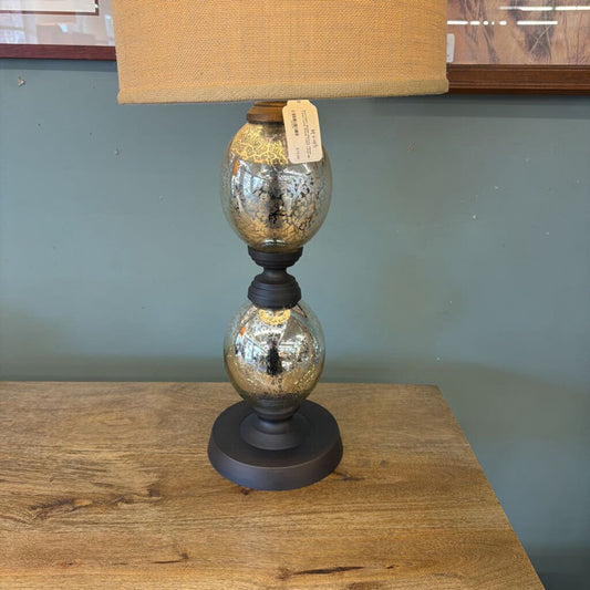 Table lamp with a textured glass base and beige lampshade on a wooden surface.