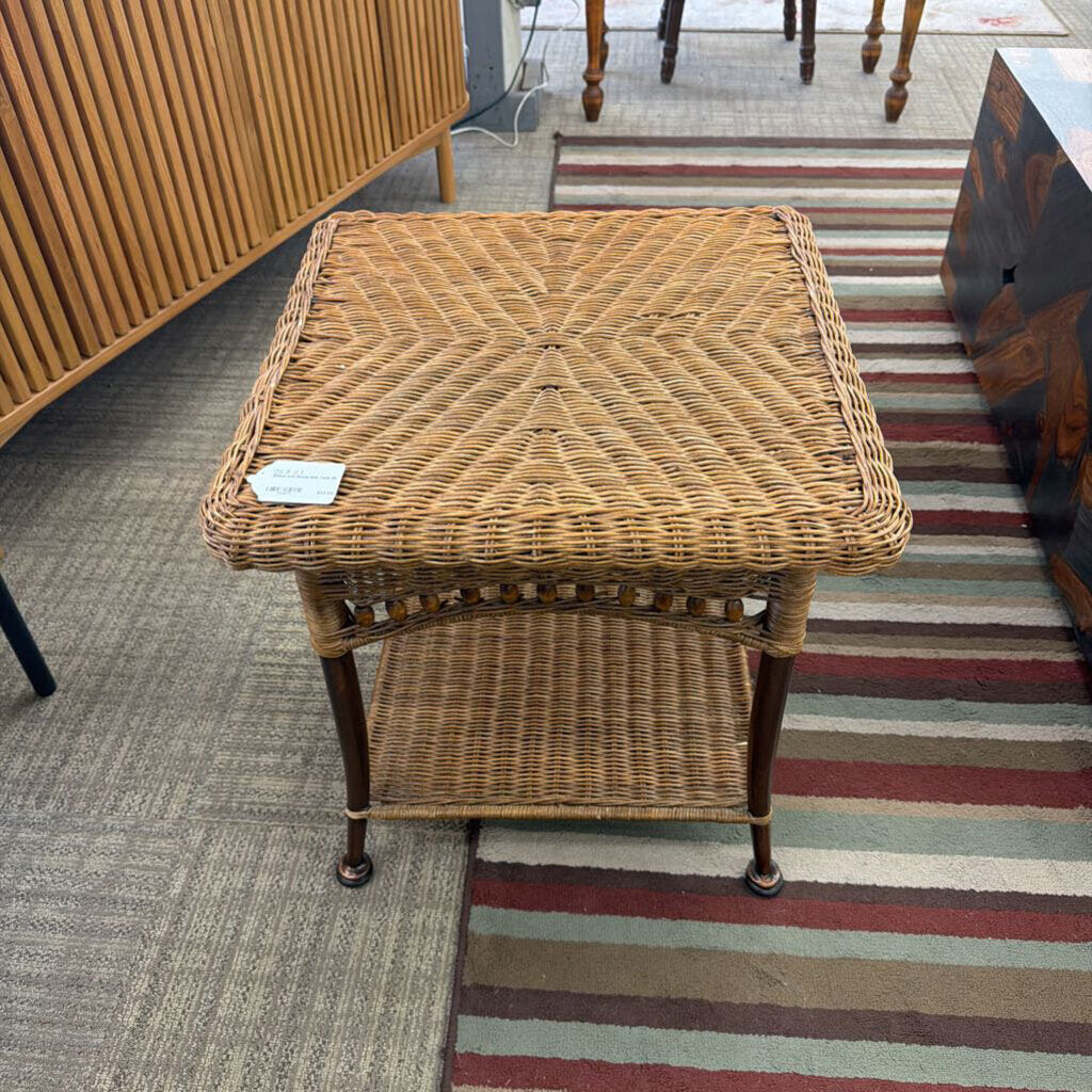 Wicker side table on a striped rug with a wooden cabinet in the background