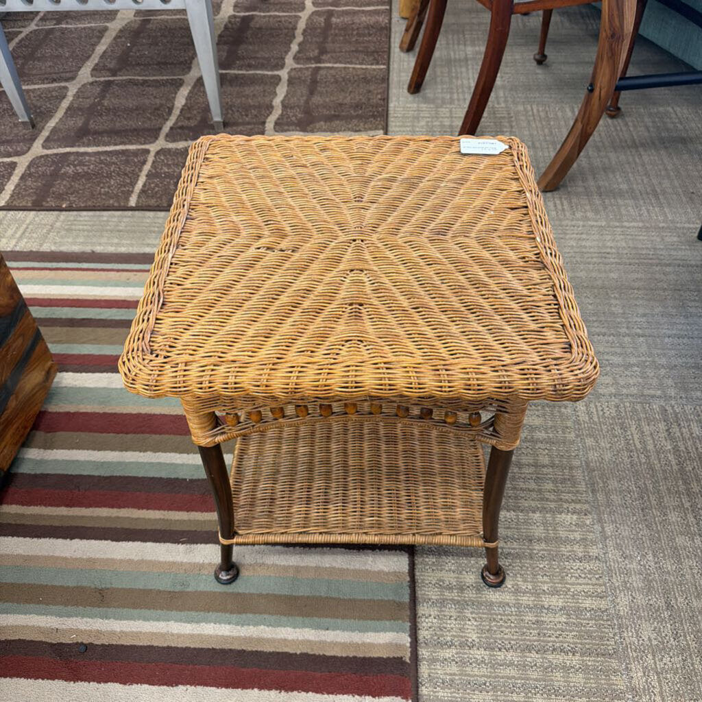 Wicker side table on a carpeted floor with a striped rug