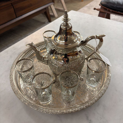 Silver teapot and glass set on a decorative tray with a marble surface background