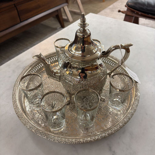 Silver teapot and glass set on a decorative tray with a marble surface background